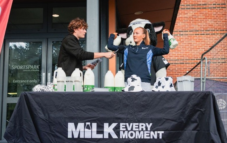 Two students and Moovit the cow mascot at the Milk Every Moment dairy stand.